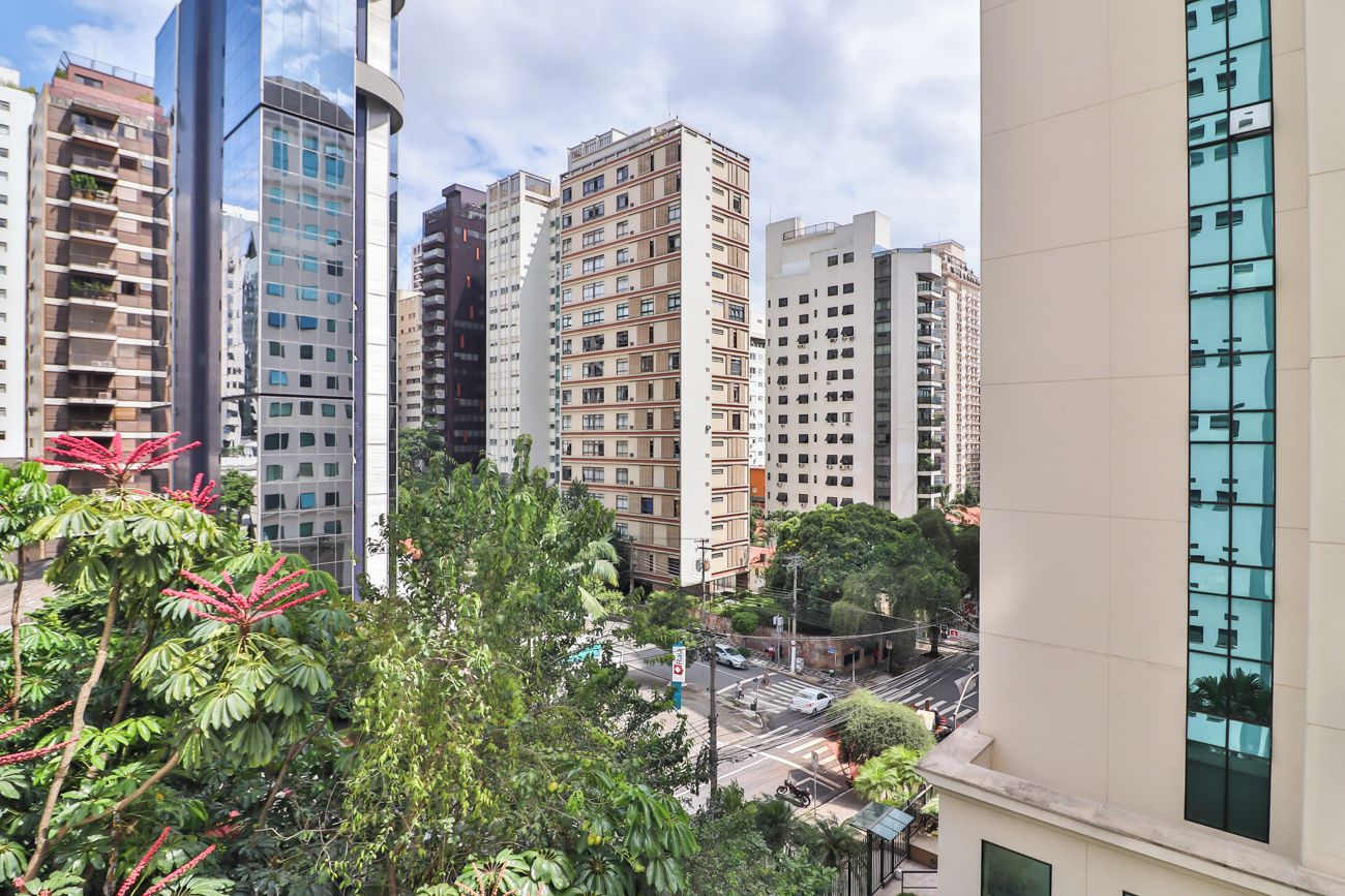 Um edifício alto com vários andares, cercado por outros edifícios altos e uma rua com veículos.