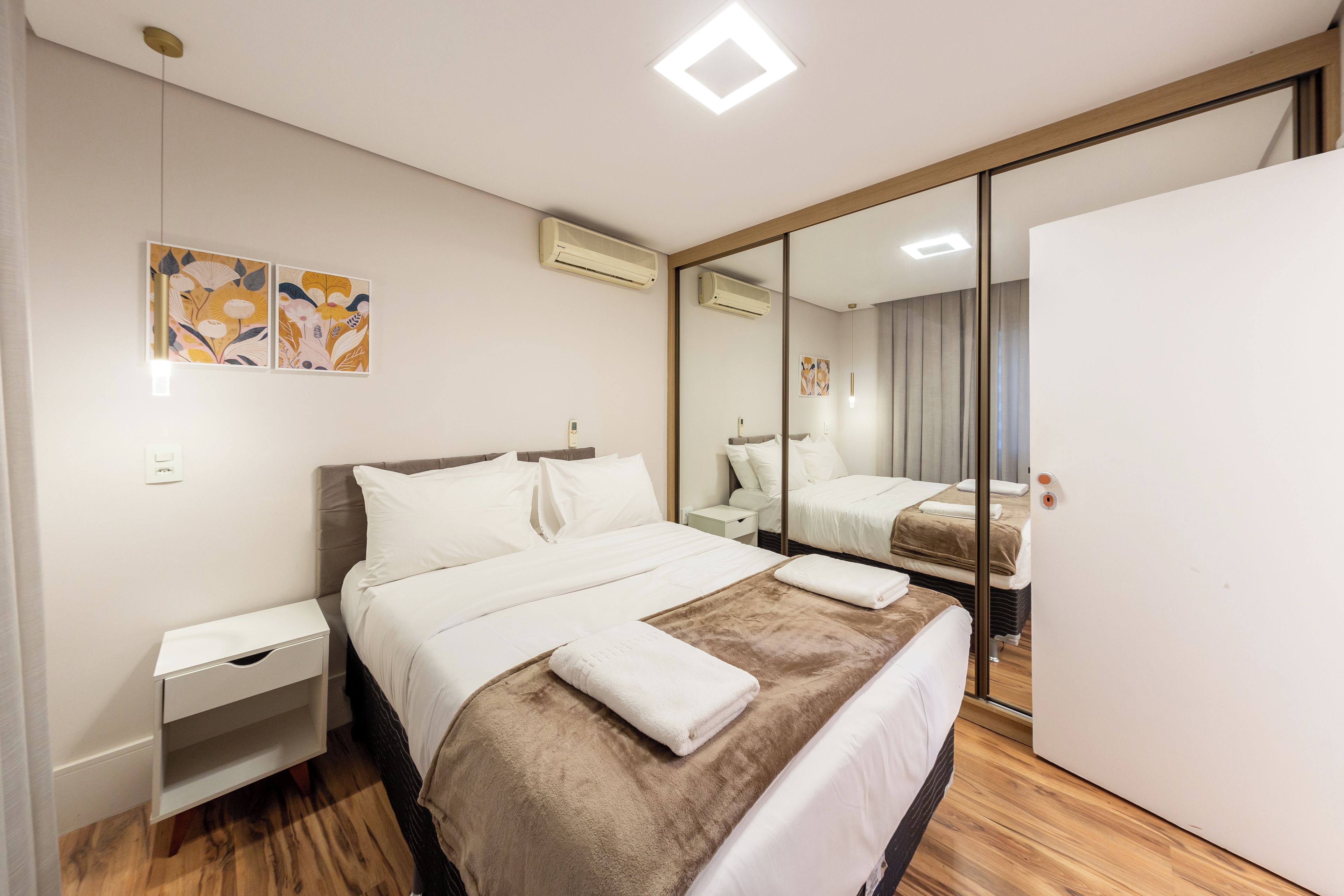 Quarto de hotel com cama, mesas de cabeceira, guarda-roupa e espelho.