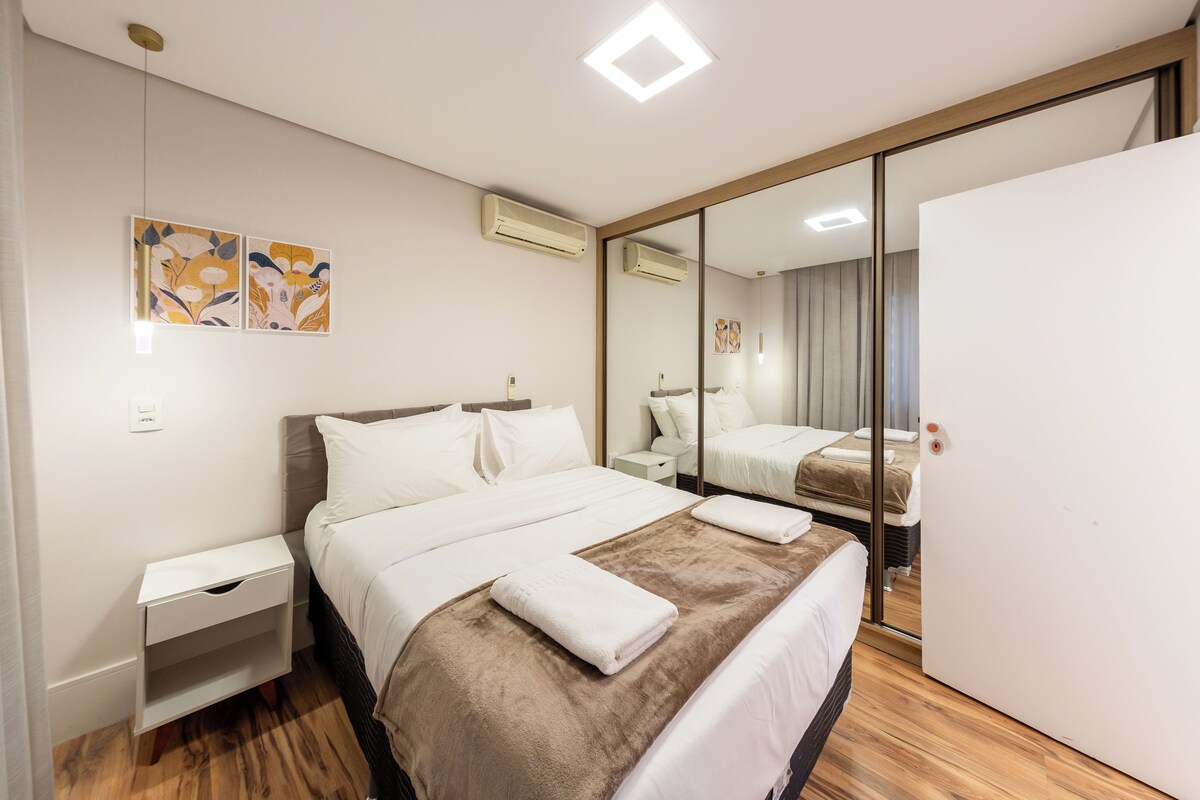Quarto de hotel com cama, mesas de cabeceira, guarda-roupa e espelho.