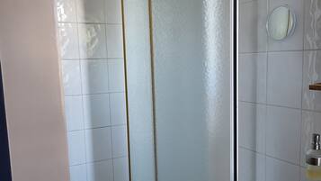 Een badkamer met een douchecabine van glas, witte tegels, een houten wastafelmeubel en een ronde spiegel.