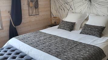 A bedroom with a large bed, a bench, a wall art piece, and a patterned wall.
