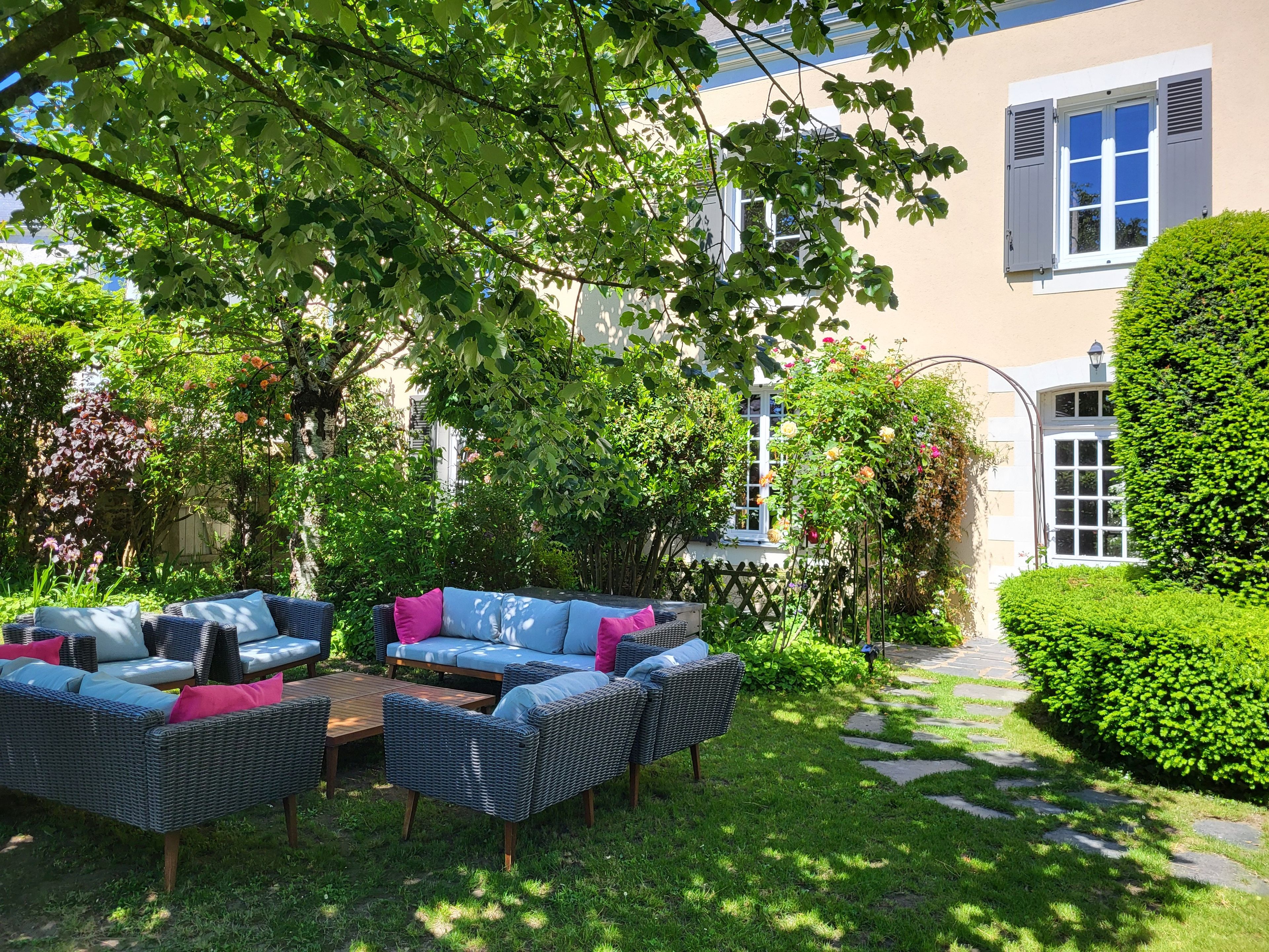 A garden with a wicker sofa set, a stone pathway, and a well-maintained hedge.