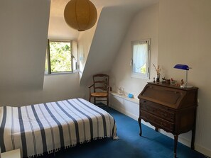 Ein Schlafzimmer mit einem Bett, einem Sessel, einem Schminktisch und zwei Fenstern.