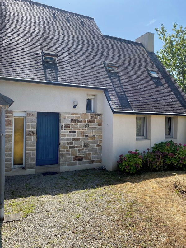 Ein Haus mit einer Stein-Fassade, einer blauen Tür und einer Zuwegung mit Kies.