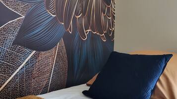 Un lit avec une couverture à motifs, un oreiller foncé et un mur orné d’une fresque florale détaillée.