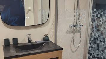 A bathroom with a black sink, wooden vanity, and a glass shower enclosure.
