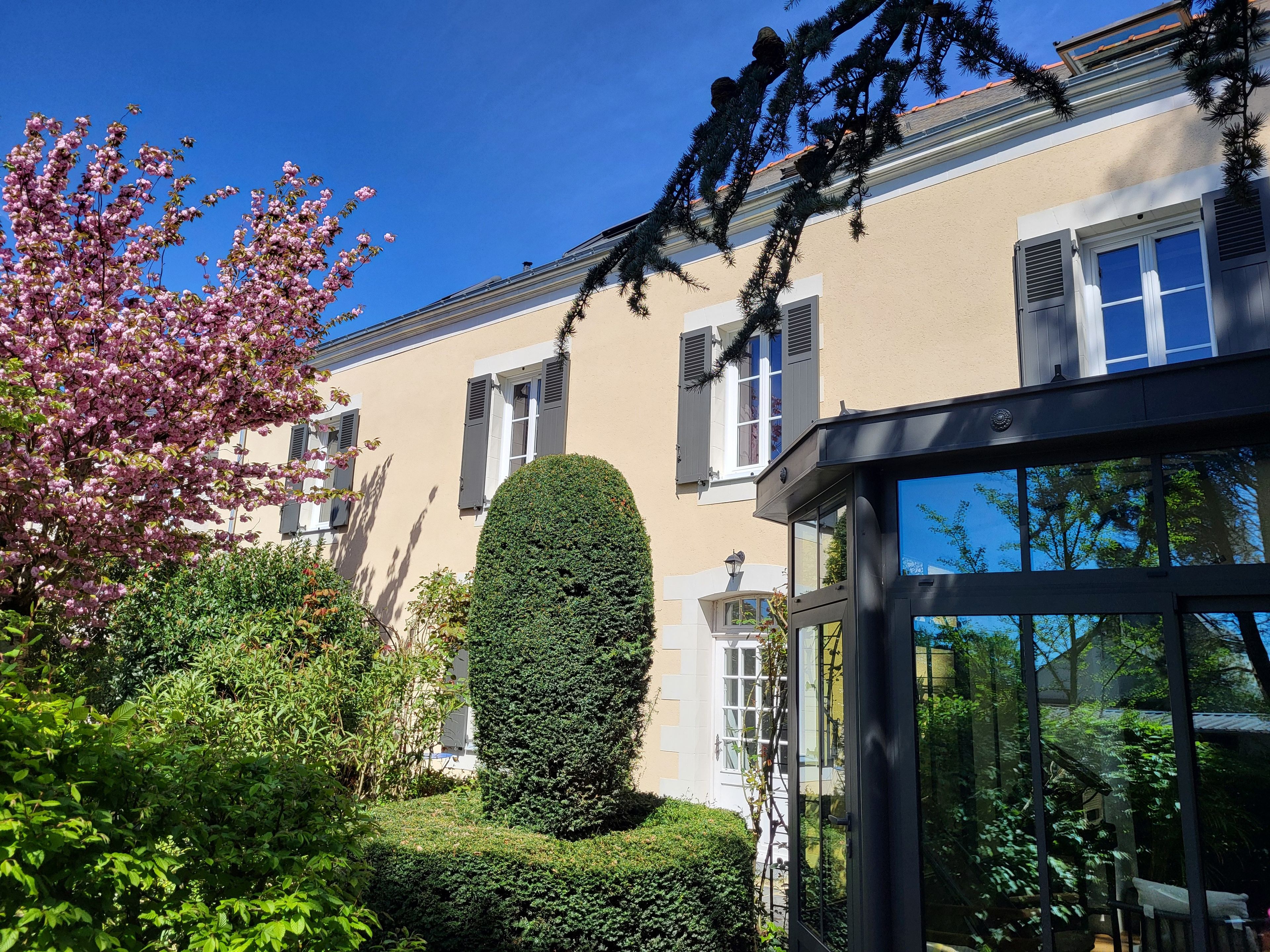 Un immeuble résidentiel doté d’un jardin bien entretenu, d’une haie soigneusement taillée et surplombant un ciel bleu dégagé.