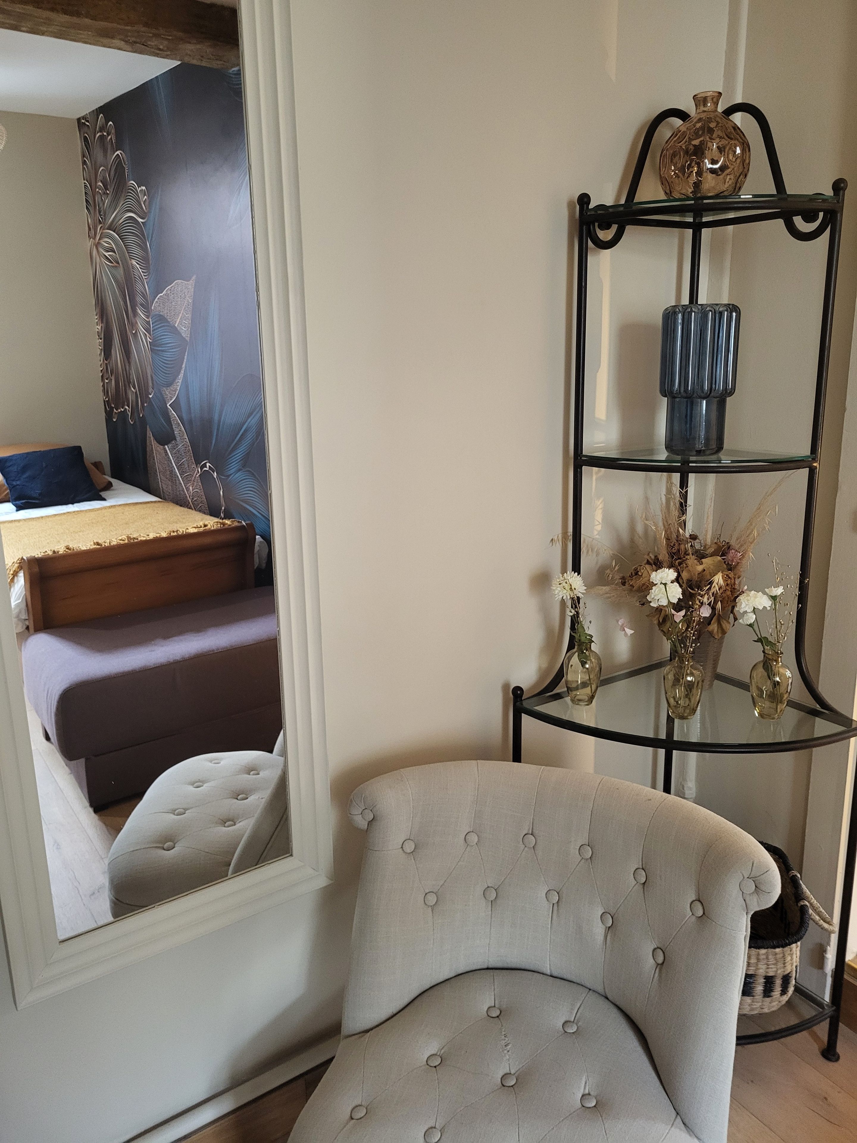 Une pièce comprenant un lit, une chaise, une étagère décorative avec des vases et un mur orné d’une tapisserie à motifs floraux.