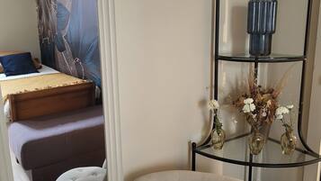 Une pièce comprenant un lit, une chaise, une étagère décorative avec des vases et un mur orné d’une tapisserie à motifs floraux.