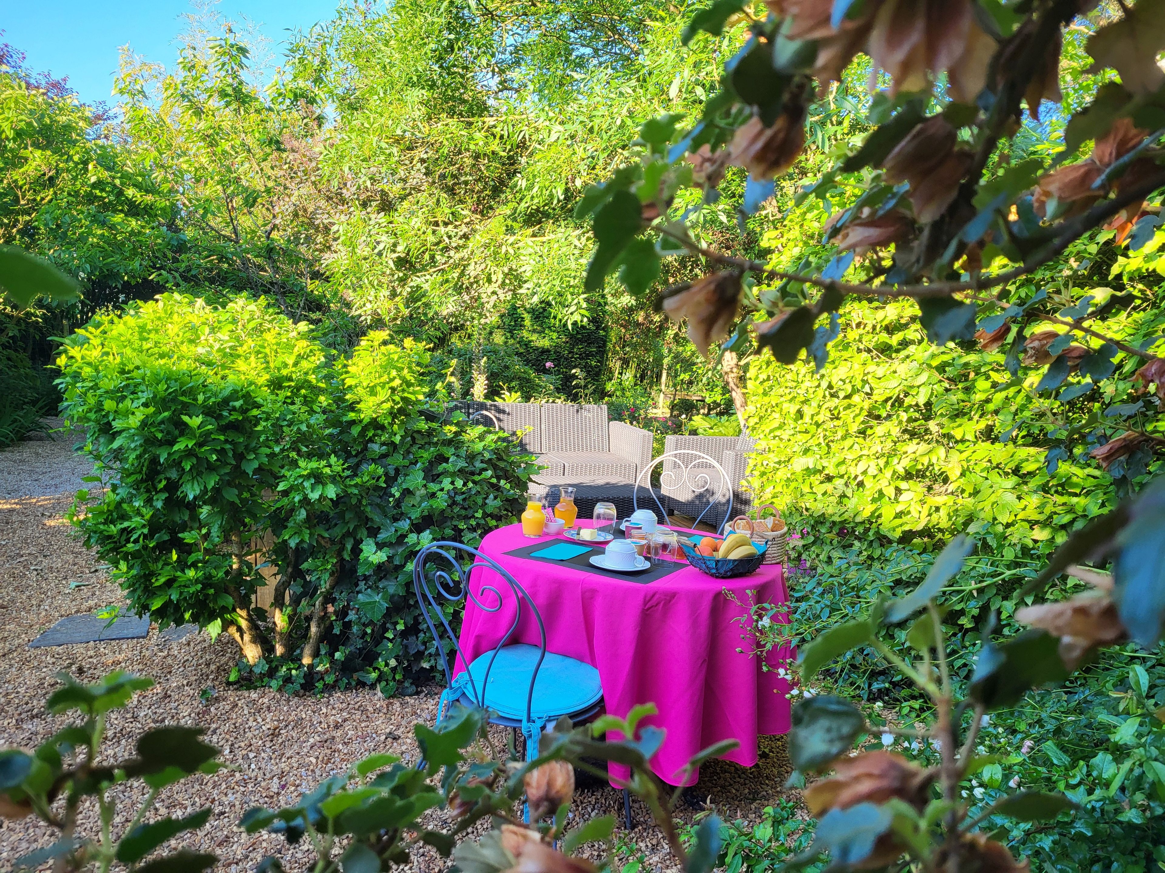 Un espace de restauration en plein air avec une table dressée pour deux personnes, entouré d’une végétation luxuriante.