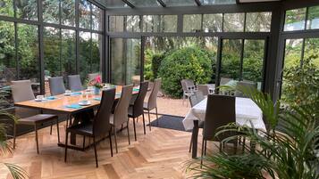 Une véranda dotée d’un plancher en bois disposé en motif de chevron, de murs en verre et d’une table dressée pour le repas.