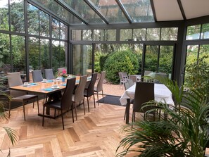 Ein Wintergarten mit Holzboden im Fischgrätmuster, Glaswänden und einem für das Essen gedeckten Tisch.