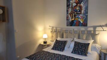 A bedroom with a bed, pillows, a nightstand with a lamp, and a painting on the wall.