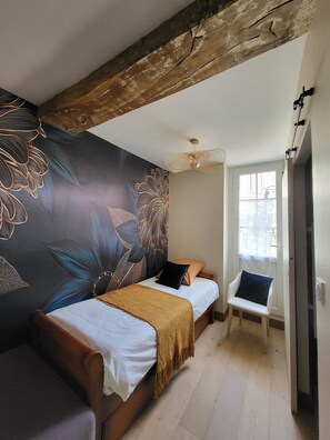 Ein Schlafzimmer mit zwei Betten, einem Holzbalken an der Decke, Wandmalerei, Deckenventilator und einem Fenster.
