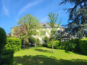 Ein großes Haus mit einem gepflegten Garten, einer Rasenfläche und verschiedenen Bäumen.