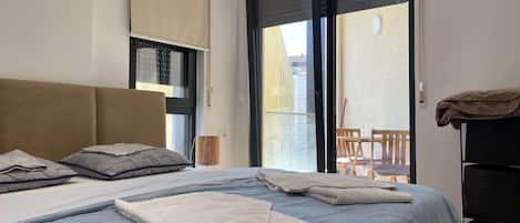 A hotel room with a bed, a chair, a table, and a balcony.