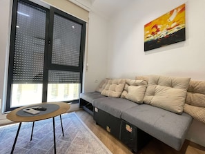 Un soggiorno con un divano grigio, un tavolino rotondo con un telecomando e un quadro appeso al muro.