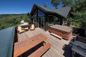 A wooden deck with outdoor seating, a hot tub, and a glass-enclosed room with a view of the surrounding landscape. - Scenic Ridge Home with Panoramic Mountain Views near Alpine, Utah (Alpine)
