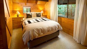 A wooden cabin bedroom with a bed, bedside lamps, and a window with curtains.