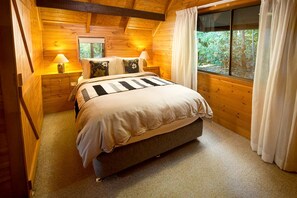 A wooden cabin bedroom with a bed, bedside lamps, and a window with curtains.