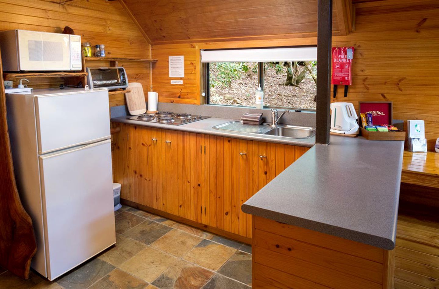 A compact kitchen with a refrigerator, microwave, stove, sink, and wooden cabinets.