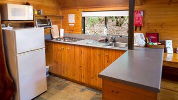 A compact kitchen with a refrigerator, microwave, stove, sink, and wooden cabinets.