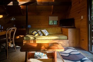 Un interior acogedor de cabaña con un sofá, un televisor y una zona de comedor.