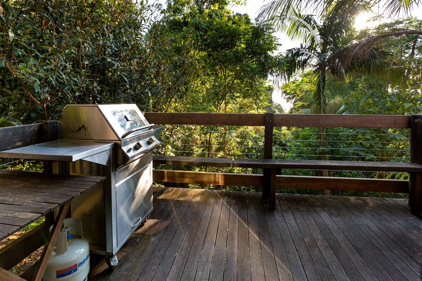 An outdoor grill area with a wooden deck, surrounded by lush greenery.