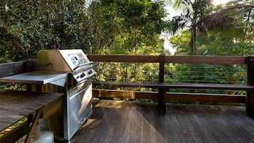 An outdoor grill area with a wooden deck, surrounded by lush greenery.