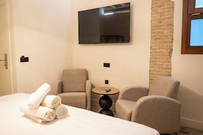 Ein Hotelzimmer mit einem Bett, zwei Sesseln, einem kleinen runden Tisch, einem flachbildfernseher an der Wand und einer Wandverkleidung aus Ziegelsteinen.