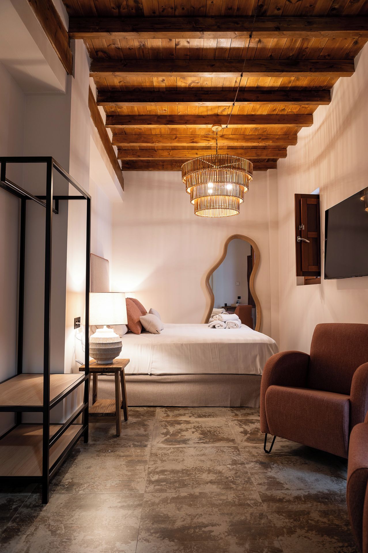 Un dormitorio con cama, mesita de noche, lámpara, silla y un espejo en la pared.