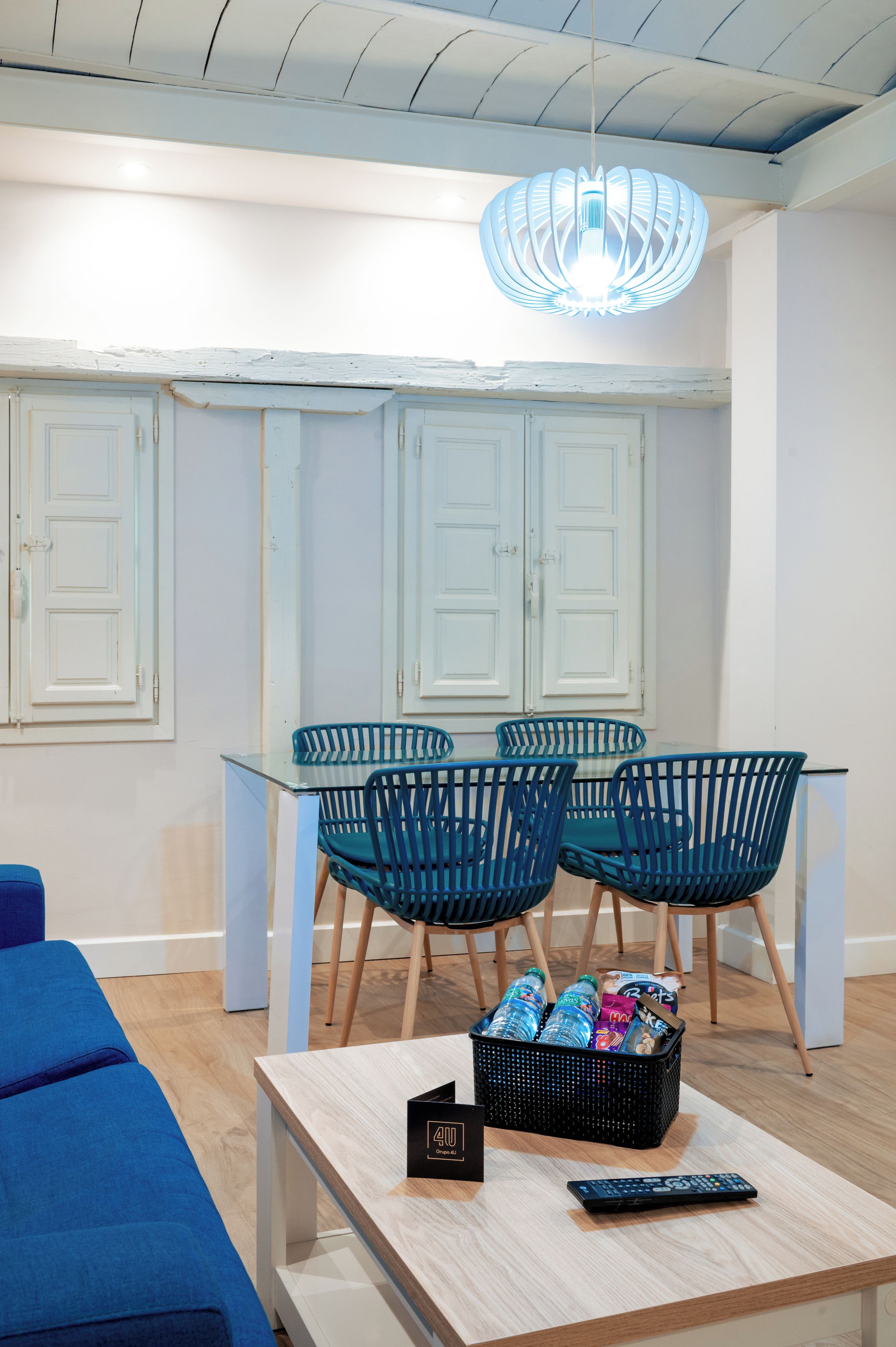 Un interior moderno con un área de comedor que presenta sillas azules, una mesa de vidrio y una cesta negra con objetos.