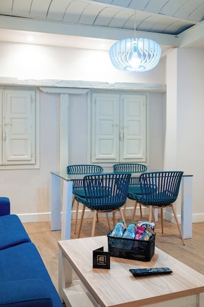 Ein modernes Interieur mit einem Essbereich, der blaue Stühle, einen Glastisch und einen schwarzen Korb mit Gegenständen zeigt.