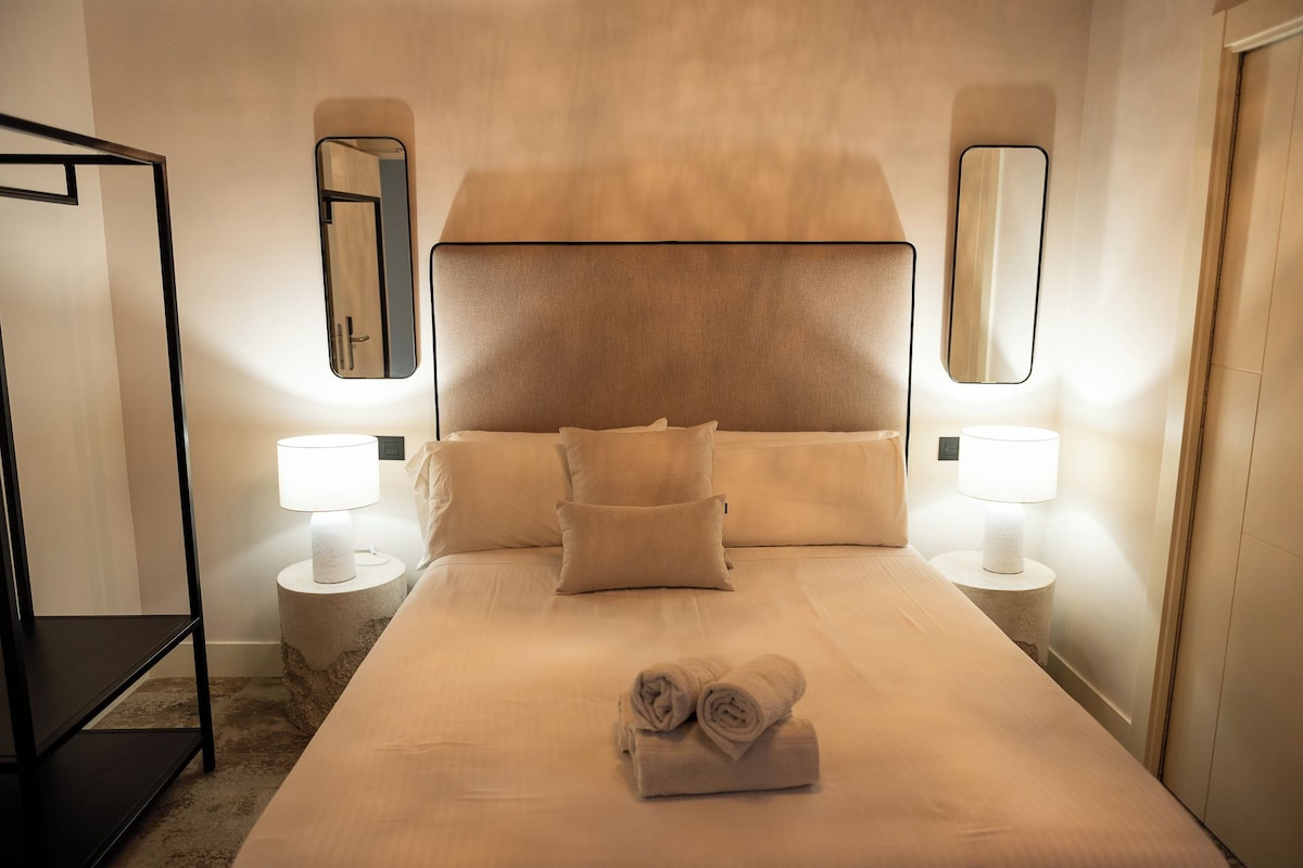 Ein Hotelzimmer mit einem großen Bett, zwei Nachttischlampen, einem Kopfteil und einem Spiegel an der Wand.