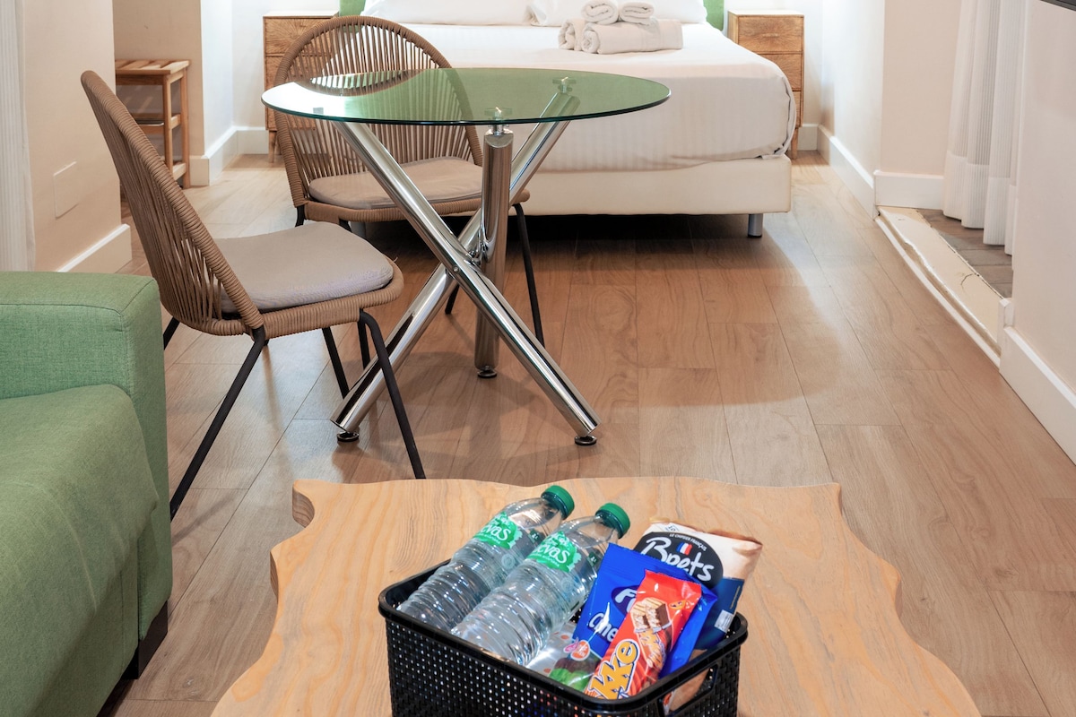 Ein Hotelzimmer mit einem Bett, einem Esstisch, einem Sessel, einem Fernseher und einem kleinen Tisch mit Snacks.