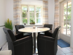 A dining area with a round table, four chairs, a window with curtains, and a potted plant on the windowsill. - 2 - Rungholtstrasse 3c (Wyk auf Foehr)