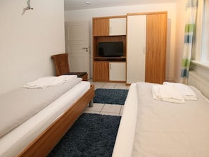A bedroom with two single beds, a wooden wardrobe, a television, and a small seating area. - 2 - Rungholtstrasse 3c (Wyk auf Foehr)
