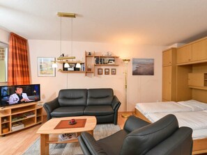 A modern living room with a sofa, a coffee table, a TV, and a bed. - 4 in the House Strandlauferweg 10 (St. Peter-Ording)
