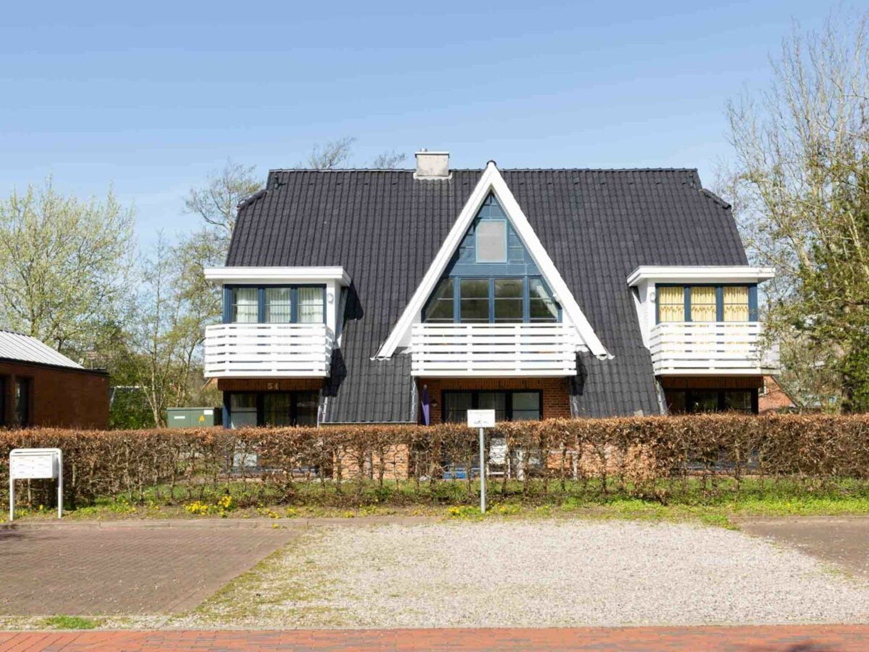 A two-story house with a dark roof, white balconies, and a brick facade.