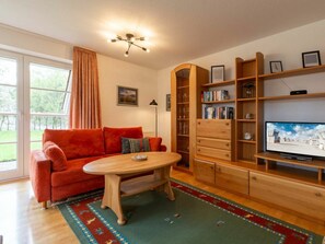 A living room with a red sofa, a wooden coffee table, a bookshelf, and a television. - Apartment 1 "dune Dream" (St. Peter-Ording)