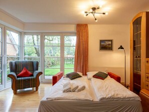 A hotel room with a large bed, a chair, a desk, and a view of the outdoors. - Apartment 1 "dune Dream" (St. Peter-Ording)
