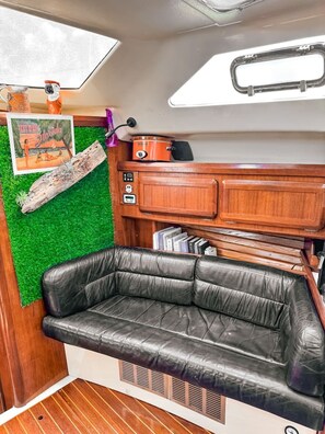 A compact living space with a leather couch, a small wooden cabinet, and a poster on the wall. - Sailboat Stay + Resort Amenities (Key West)