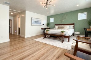 Een slaapkamer met houten vloer, een bed met hoofdbord, nachtkastje, lamp en wandlamp.