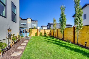 A residential backyard with a well-maintained lawn, a wooden fence, and a small garden area with plants. - Park City Views! Hot Tub, Game Room & EV Charger (Park City)