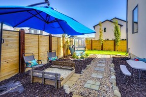 Un jardin avec une terrasse en bois, un parasol bleu et un espace aménagé pour les plantes.