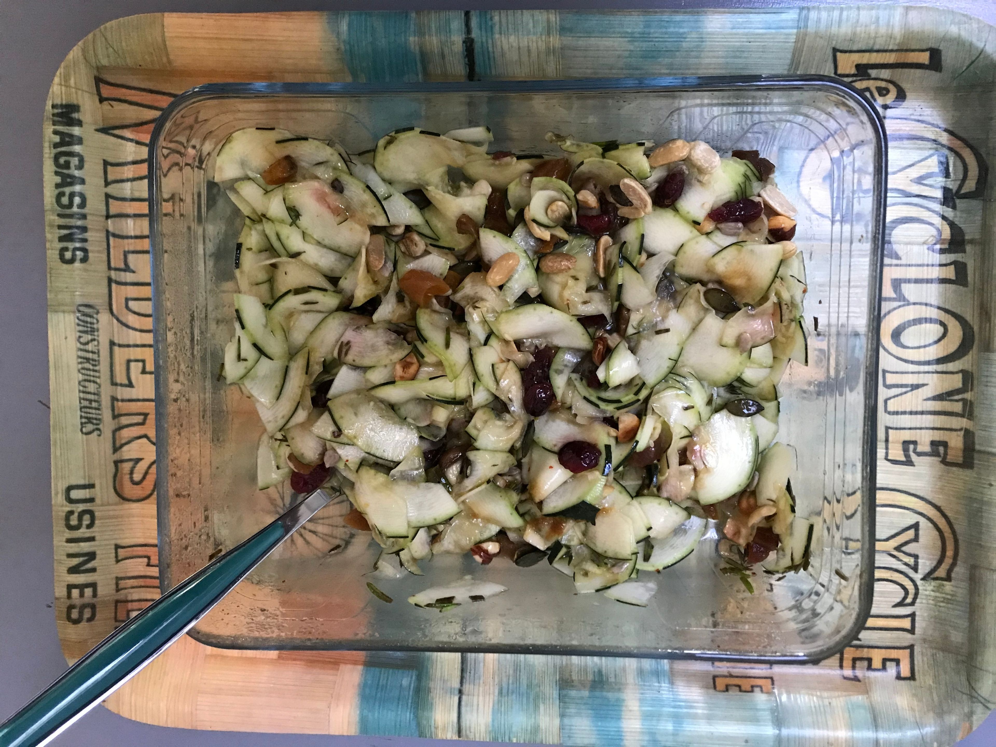 A glass container with sliced apples and nuts on a surface with a wooden pattern.