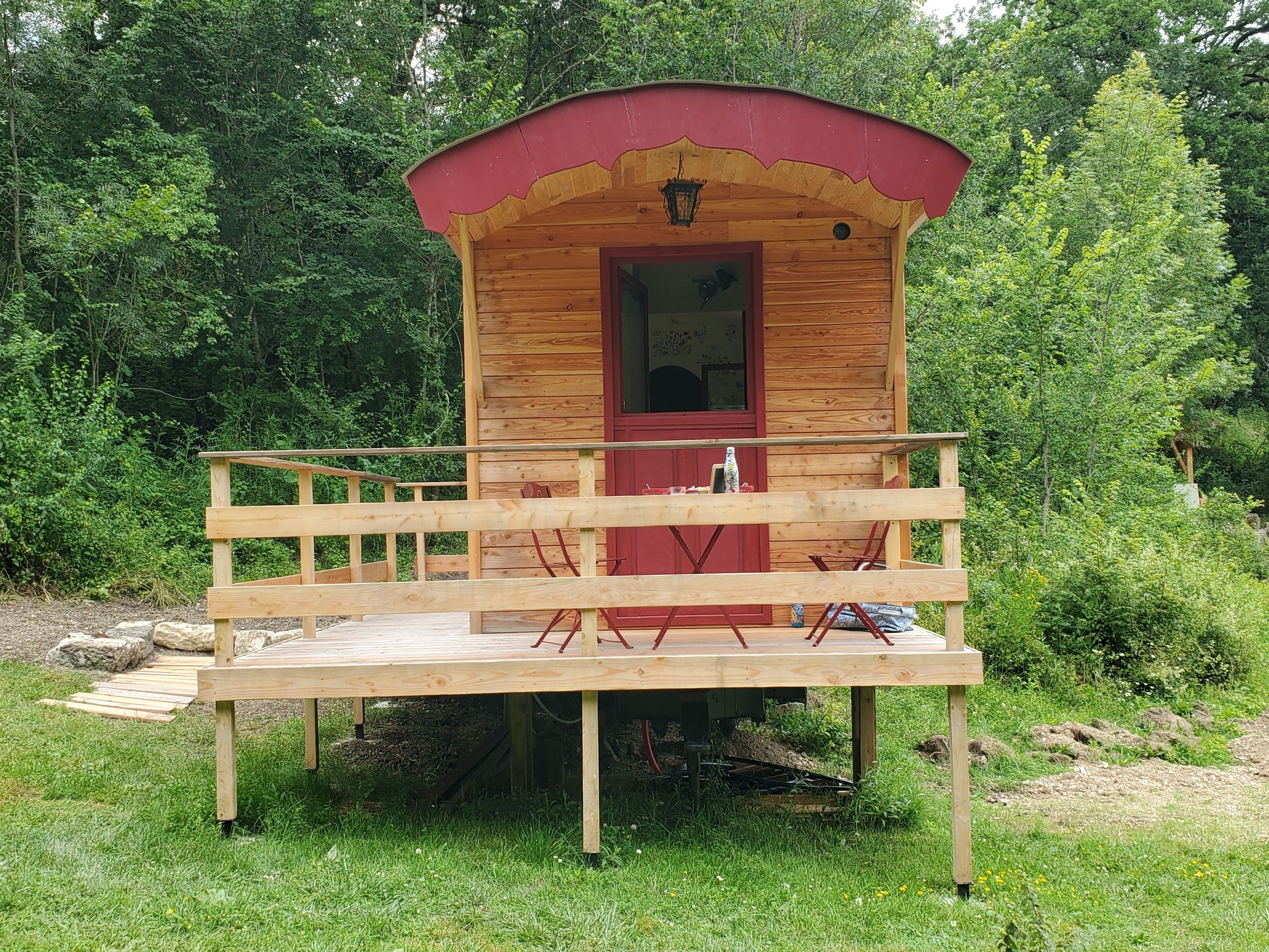 Una cabaña de madera con puerta roja y un balcón, rodeada de follaje.
