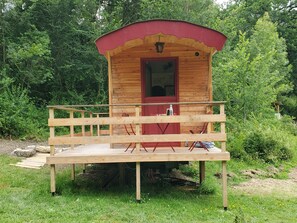 Una baita in legno con una porta rossa e un balcone, immersa nel verde.