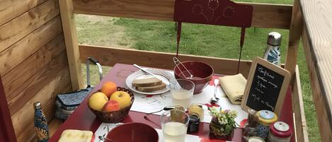 A wooden deck with a table set for a meal, including bread, fruits, and condiments.