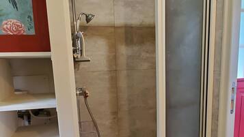 Une douche à l’italienne avec une porte en verre, un porte-serviettes et une étagère.